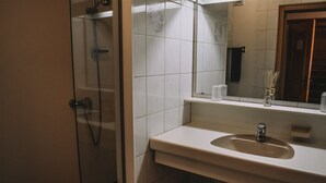 A bathroom with a glass shower enclosure, a sink with a mirror above it, and a small shelf with toiletries. - Landhaus Andrea (Saalbach-Hinterglemm)