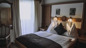 A hotel room with a large bed, wooden headboard, two bedside lamps, and a window with curtains. - Landhaus Andrea (Saalbach-Hinterglemm)