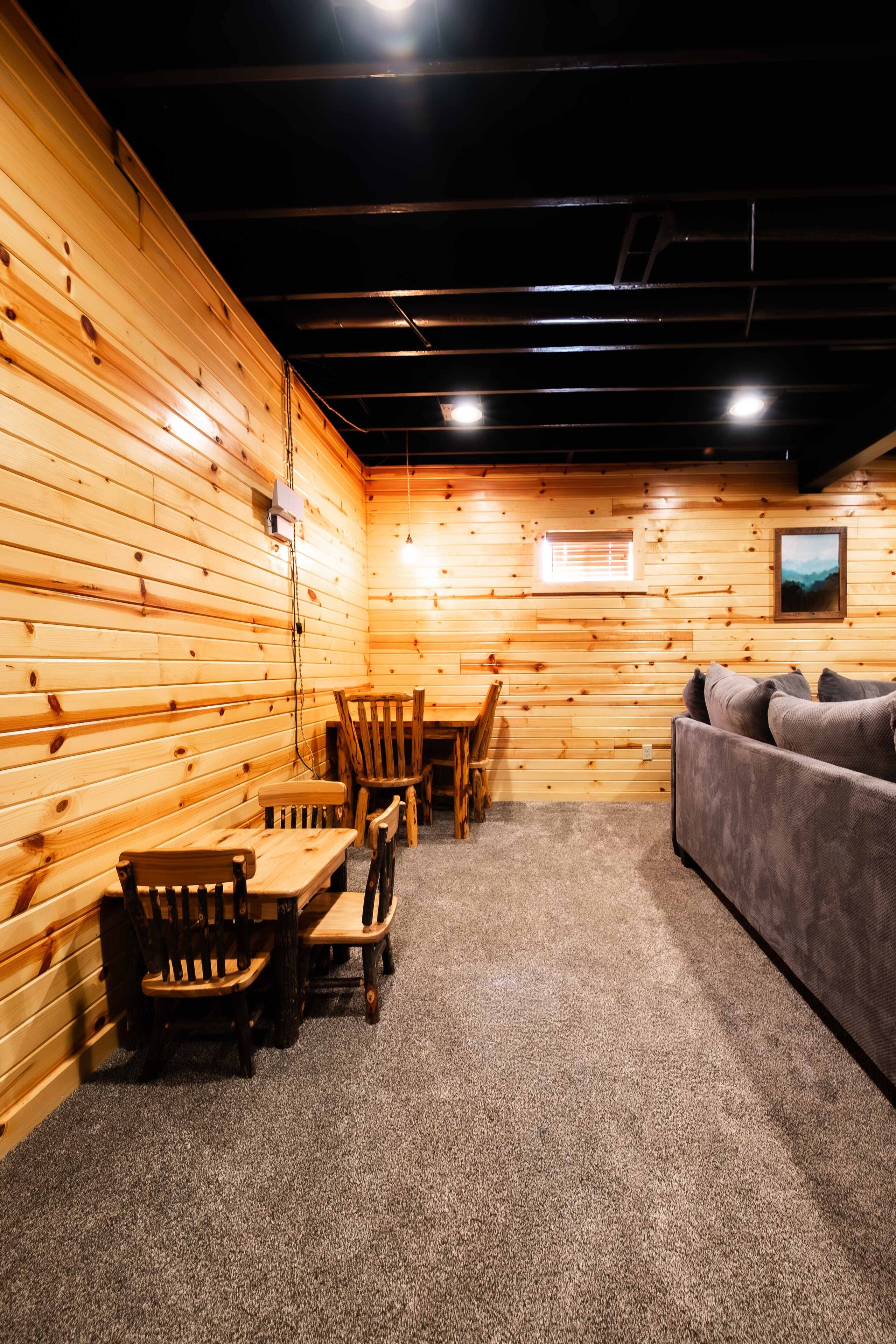 A cozy room with wooden walls, a sofa, a table with chairs, and a carpeted floor.
