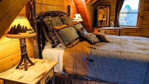 A cozy wooden cabin bedroom with a bed, a nightstand with a lamp, and a window with a view of the outdoors.