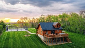 A log cabin with a deck, surrounded by a well-maintained lawn and trees.