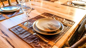 A wooden dining table with a placemat, a plate, a glass, and cutlery.