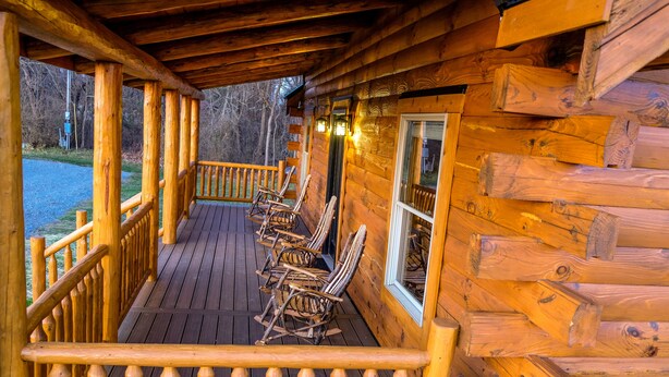 A wooden cabin with a porch, rocking chairs, and a view of the surrounding forest.