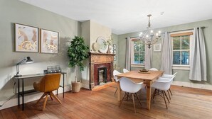 Un comedor con mesa de madera, sillas blancas, chimenea y una araña.