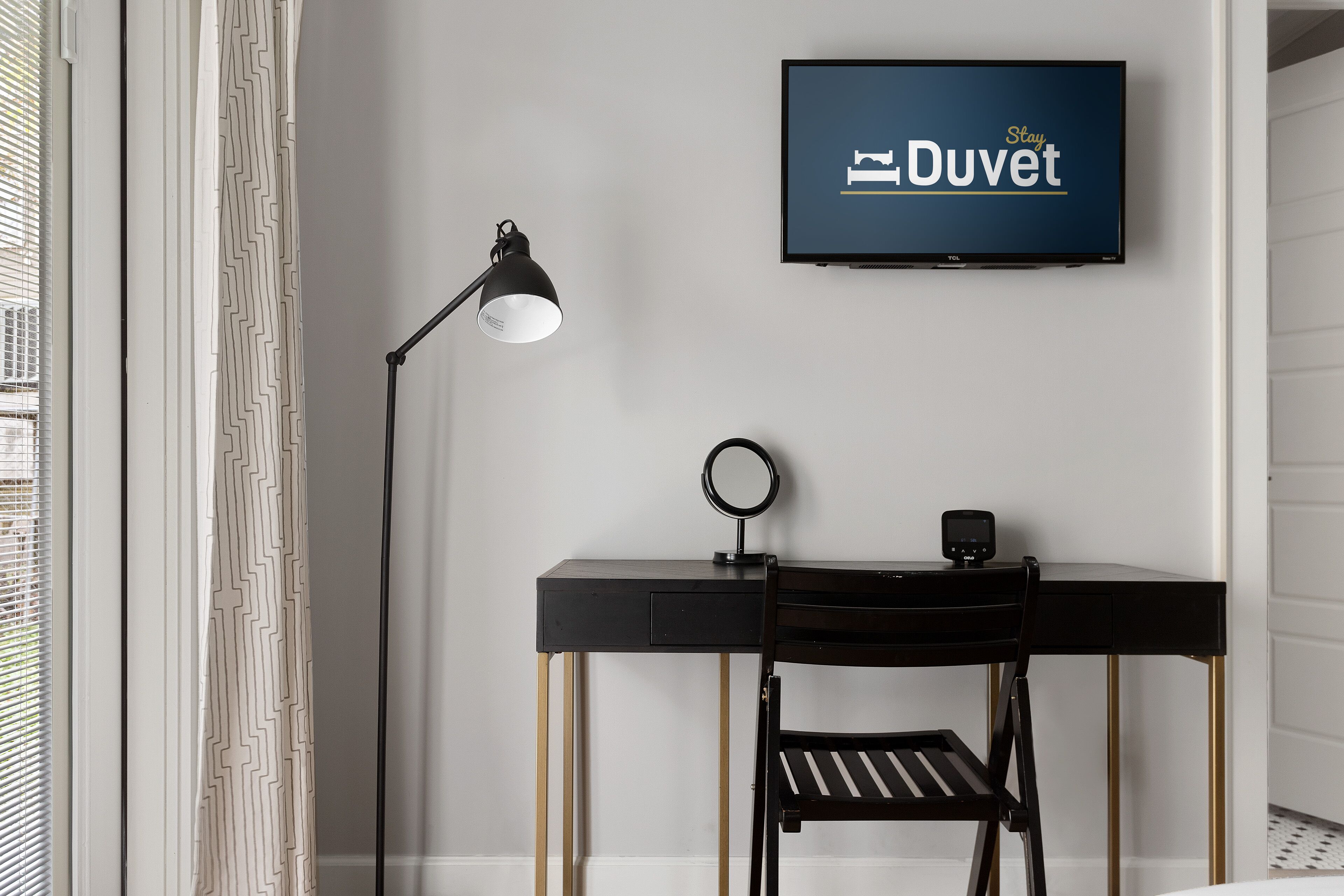 A modern room with a black desk, a ring light, a television on the wall, and a chair.