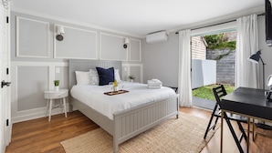 A bedroom with a bed, bedside table, and a view of the garden through a sliding door. - Only 3 Blocks from King | Backyard! | The Felix (Charleston)