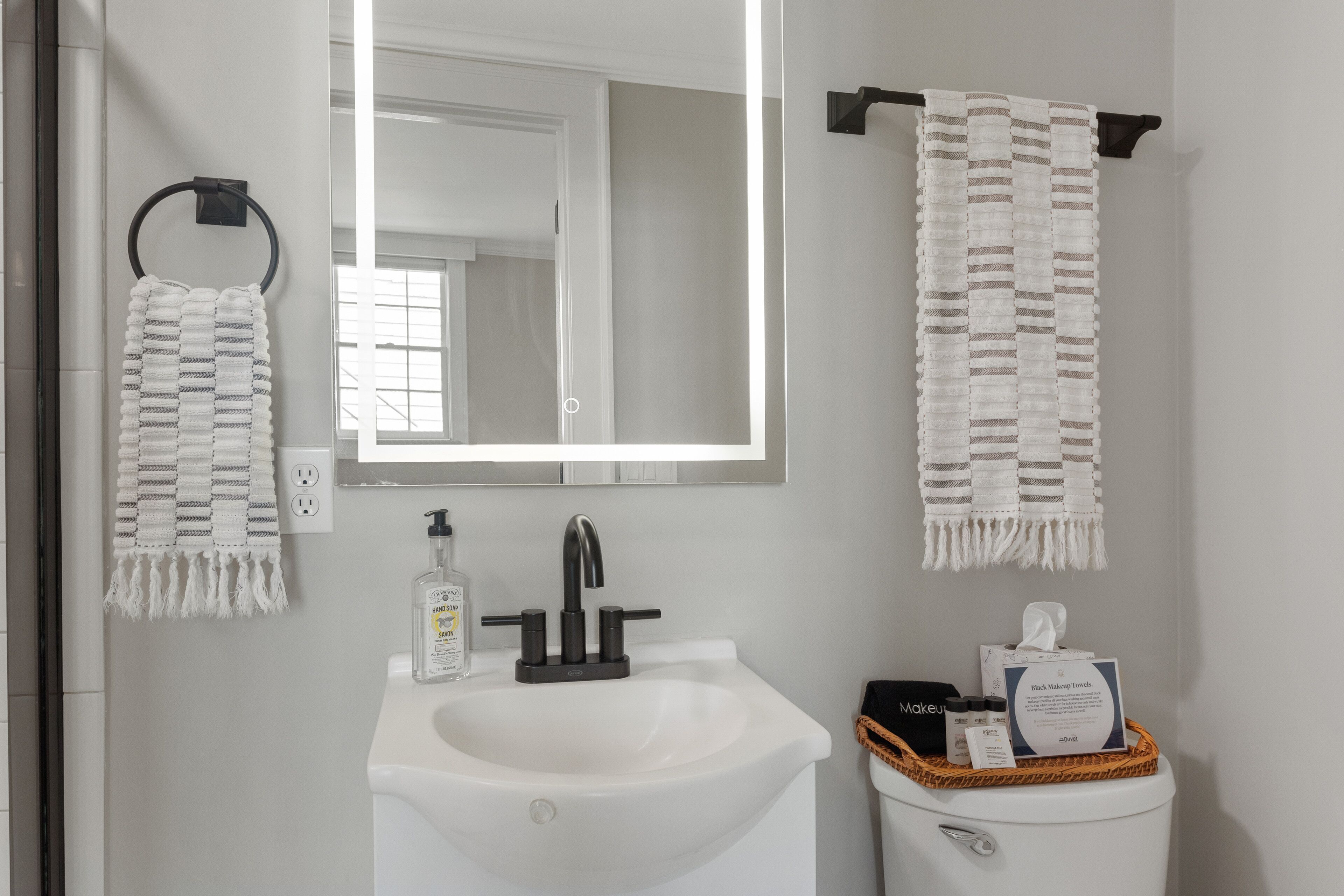 Une salle de bain avec un lavabo blanc, un miroir et deux serviettes suspendues à des porte-serviettes.