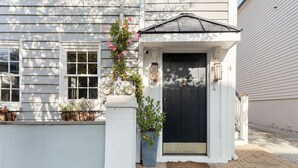 A white building with a black door, a small porch, and potted plants. - Only 3 Blocks from King | Backyard! | The Felix (Charleston)