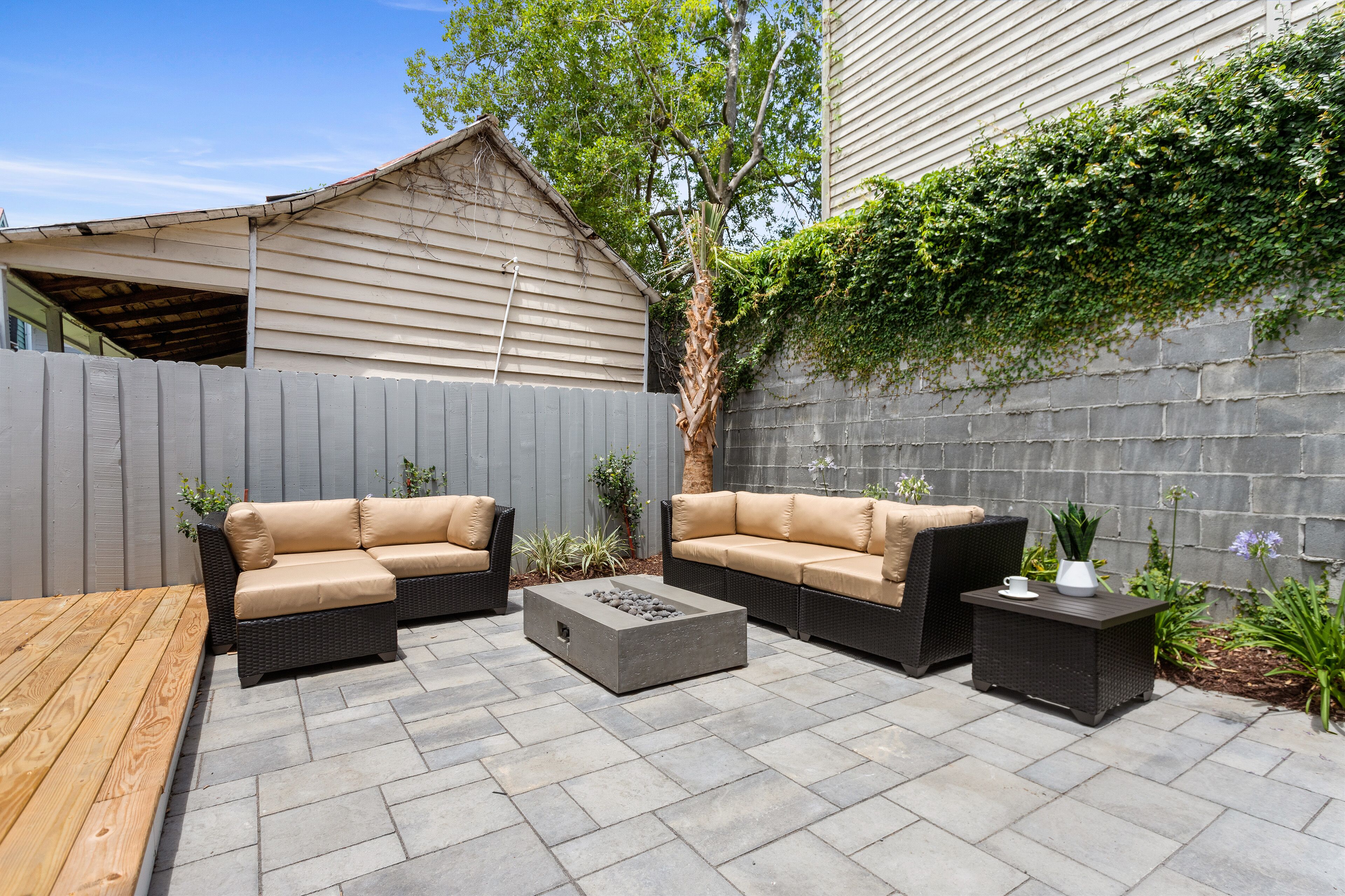 An outdoor patio area with two beige sofas, a rectangular coffee table, and a small side table with a cup and vase.