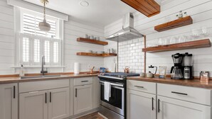 A kitchen with white cabinets, a stainless steel oven, wooden shelves, and a window with blinds. - Only 3 Blocks from King | Backyard! | The Felix (Charleston)