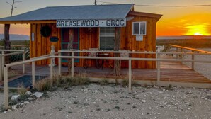 Eine Holzhütte mit einem Schild, auf dem 'GREASEWOOD - GROC' steht, und einer Holzterrasse, die zum Eingang führt.