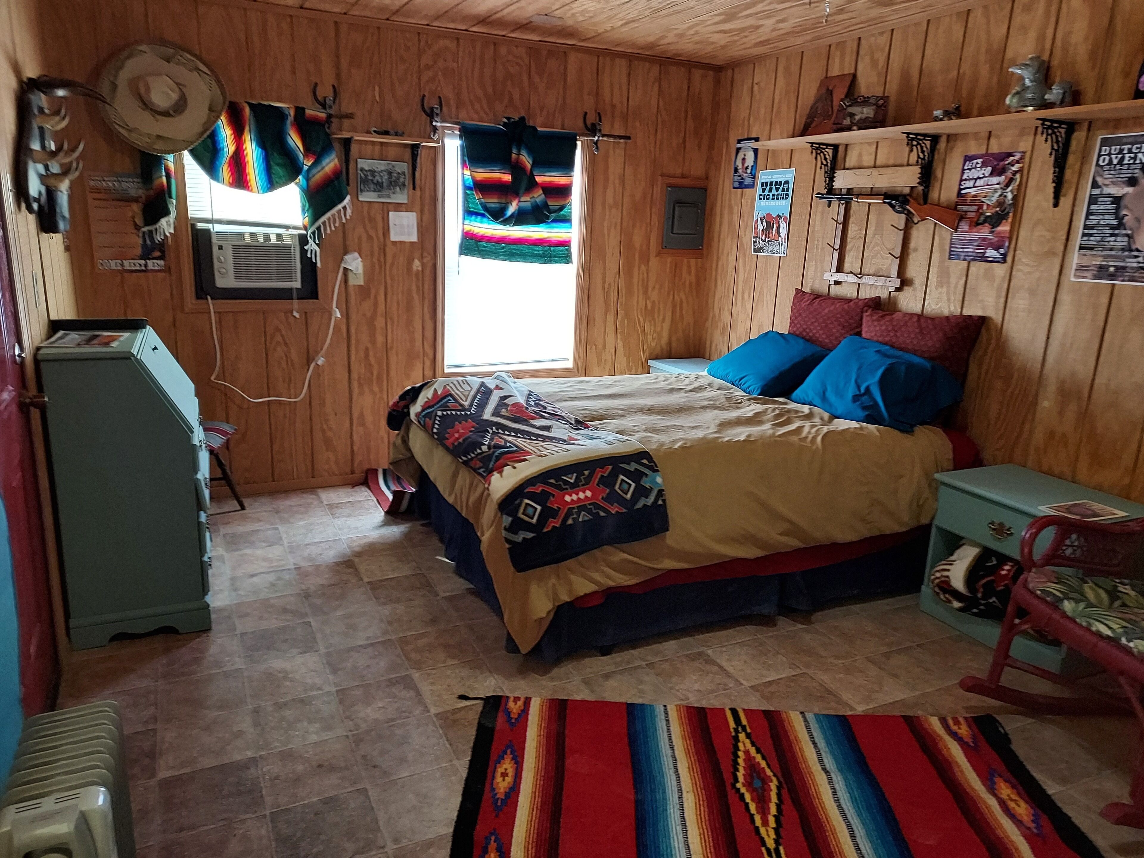 Una habitación con paneles de madera, una cama, una mesita, un radiador y un calentador fijado a la pared.
