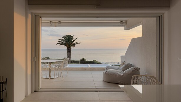 Een moderne kamer met een grote schuifglazen deur naar een balkon met uitzicht op zee en een palmboom.