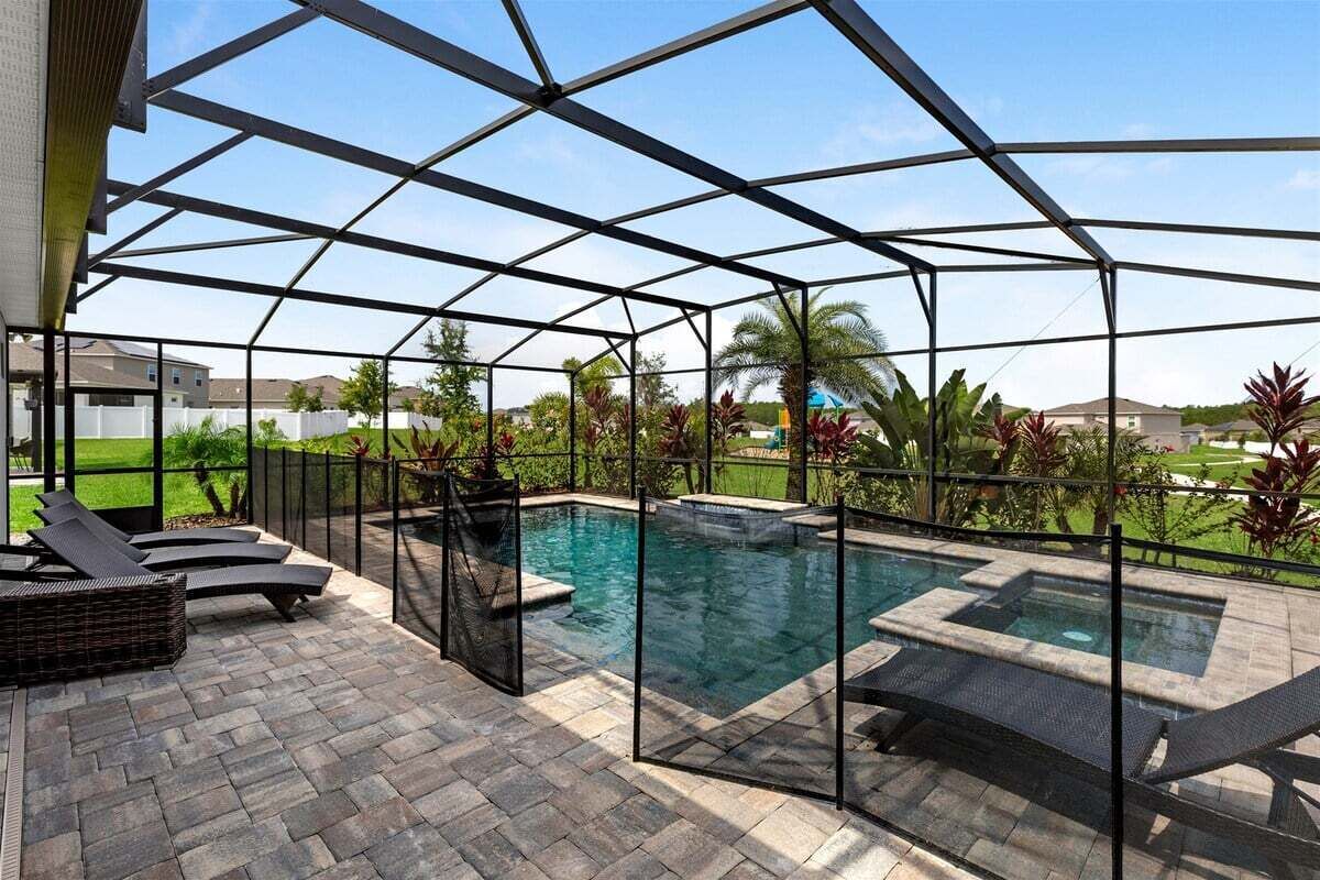 A covered outdoor swimming pool with a metal roof, lounge chairs, and a stone patio.