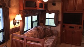 A cozy RV interior with a sofa, a TV, and wooden cabinets. - Hookem.Hideout I (Quitman)