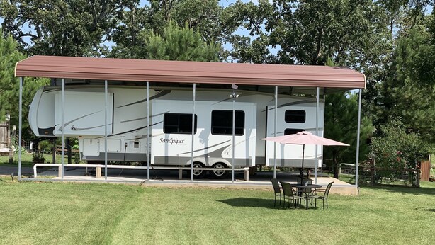 A recreational vehicle with a covered patio area, a table with chairs, and a small umbrella. - Hookem.Hideout I (Quitman)