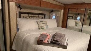 A bed with a white quilt, two folded towels, and a wooden headboard. - Hookem.Hideout I (Quitman)