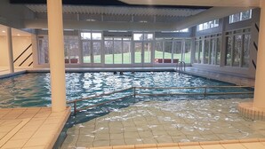 Ein Hallenbad mit klarem Wasser, umgeben von großen Fenstern und einem Fliesenboden.