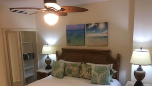 A hotel room with a bed, two bedside lamps, a ceiling fan, a nightstand with a radio, and two wall-mounted paintings of a beach and a sunset. - ON EAGLE BEACH Costa Linda Beach Resort (oranjestad)