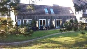 A wooden house with a sloped roof, large windows, and a patio with outdoor furniture.