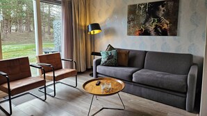 A modern living room with a grey sofa, two brown leather chairs, a round wooden coffee table with a remote control and glass, and a floor lamp.