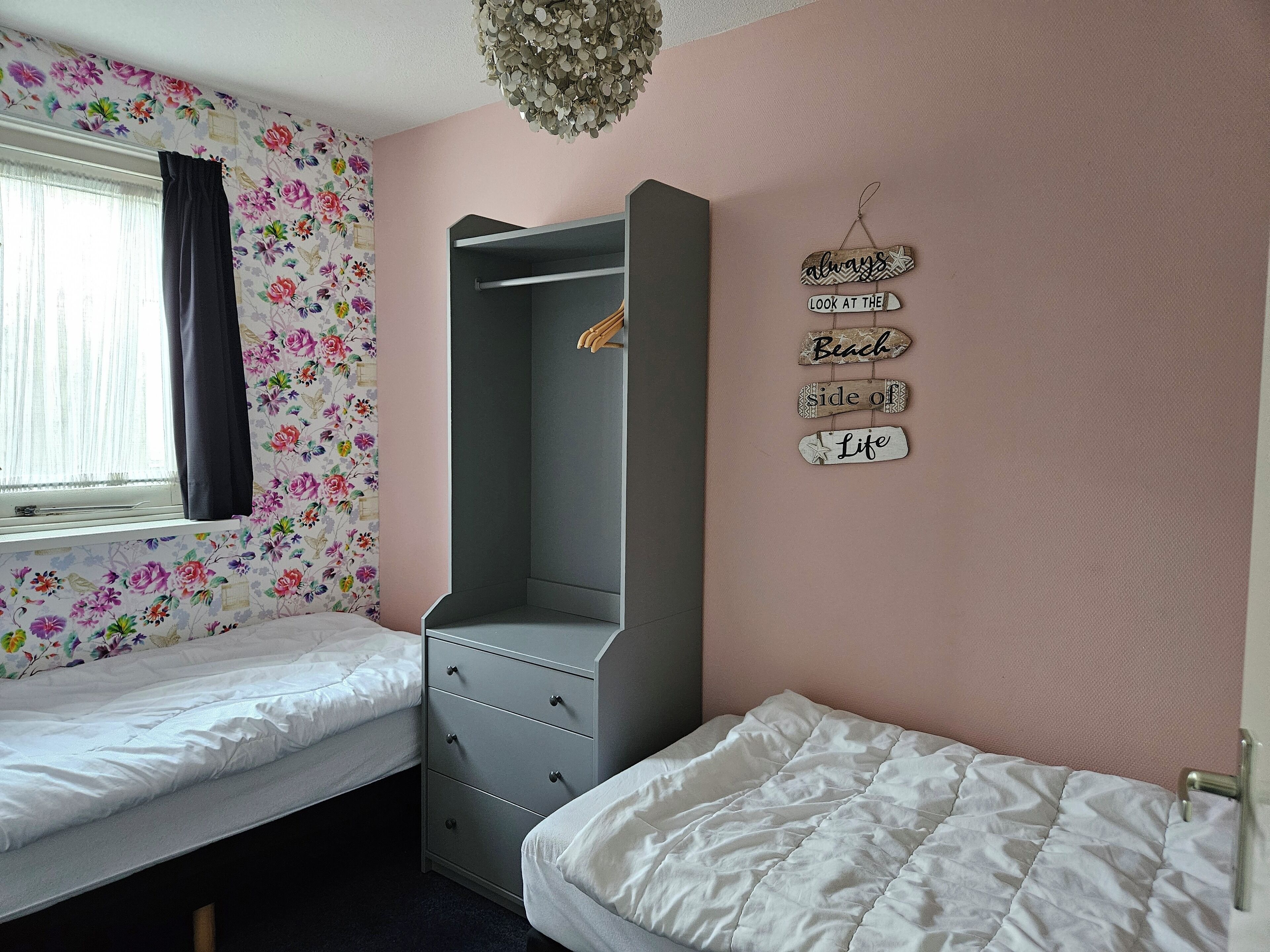 Una camera da letto con due letti singoli, un armadio grigio e una finestra con carta da parati floreale.