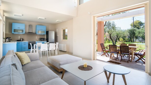 A modern living room with a sofa, a coffee table, and a dining area with chairs and a table. - Three Stars Luxury Villas (Corfu)