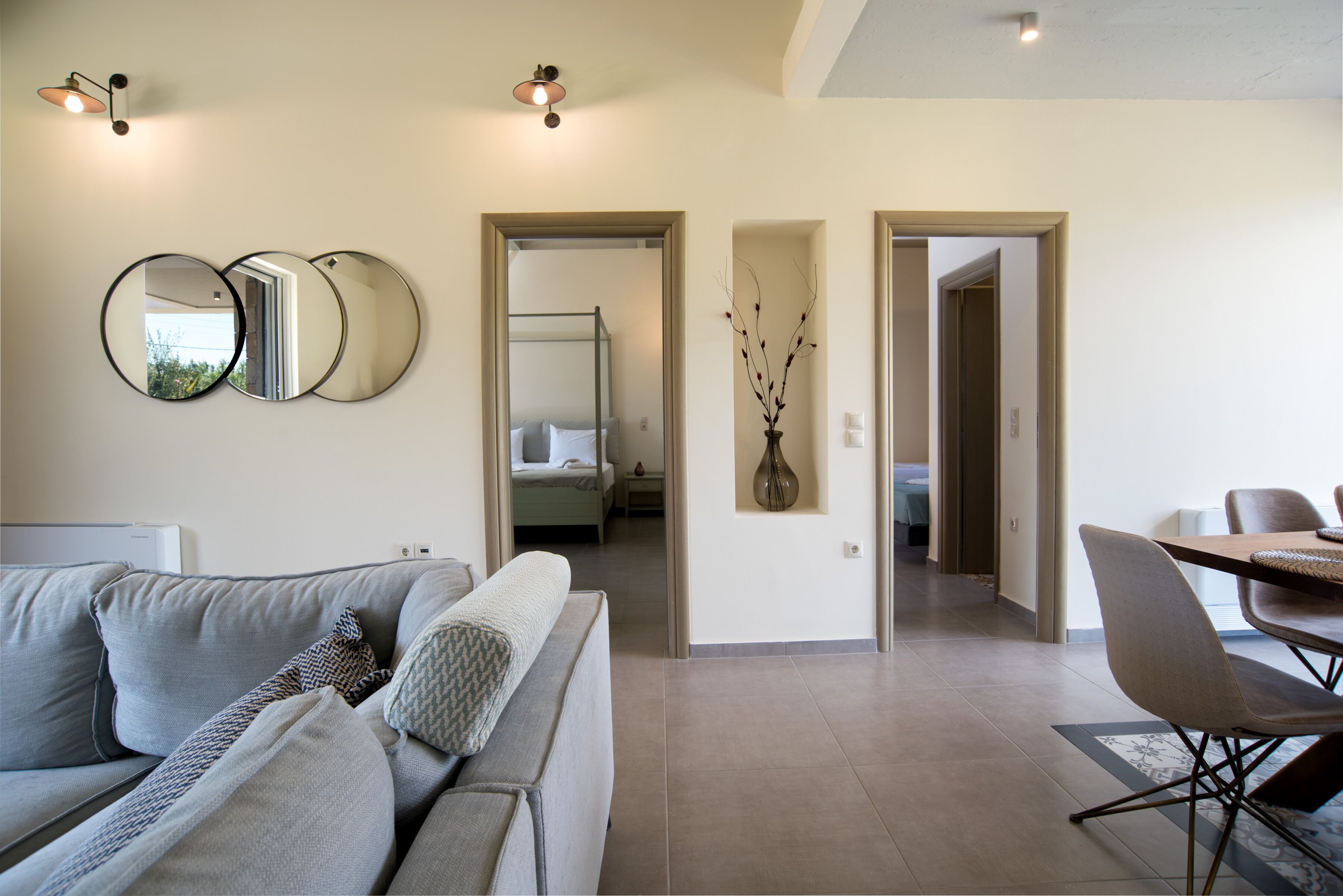 A modern living room with a sofa, a dining table with chairs, and a hallway leading to a bedroom.