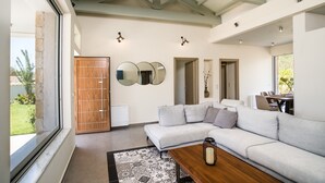 A modern living room with a sectional sofa, a wooden coffee table, and a patterned rug. There are three wall-mounted mirrors and a door leading to another room. - Three Stars Luxury Villas (Corfu)
