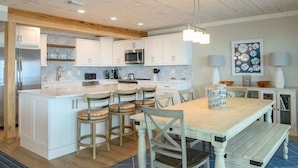 A modern kitchen with white cabinets, a central island with bar stools, a microwave, and a hanging light fixture. - On Cloud 9 | Gulf-Front, Private Beach (Santa Rosa Beach)