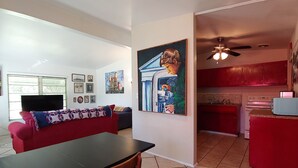 A modern living room with a red sofa, a dining table, and a kitchen area with red cabinets and a microwave. - Mid Century Charm! KSC,Port Canaveral,Cocoa and Bio-Lume Kayak,Pet Friendly! (Titusville)