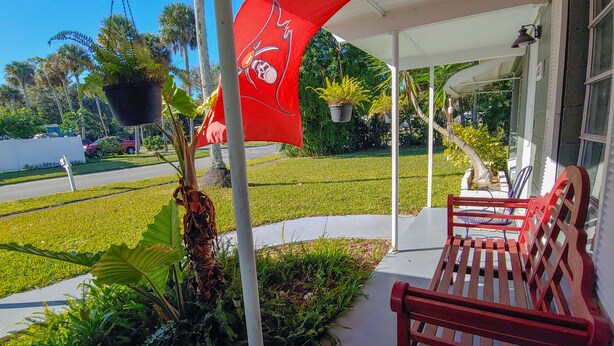 A porch with a red bench, potted plants, and a red flag with a skull and crossbones. - Mid Century Charm! KSC,Port Canaveral,Cocoa and Bio-Lume Kayak,Pet Friendly! (Titusville)