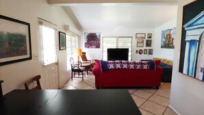 A living room with a red sofa, a TV, and a dining area with a table and chairs. - Mid Century Charm! KSC,Port Canaveral,Cocoa and Bio-Lume Kayak,Pet Friendly! (Titusville)