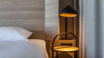 A neatly made bed with white linens, a wooden wall panel, and a modern floor lamp with a black shade.