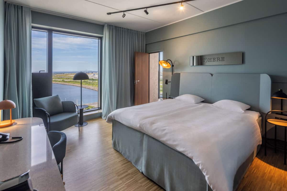 A modern hotel room with a large bed, a desk, and a view of the sea.