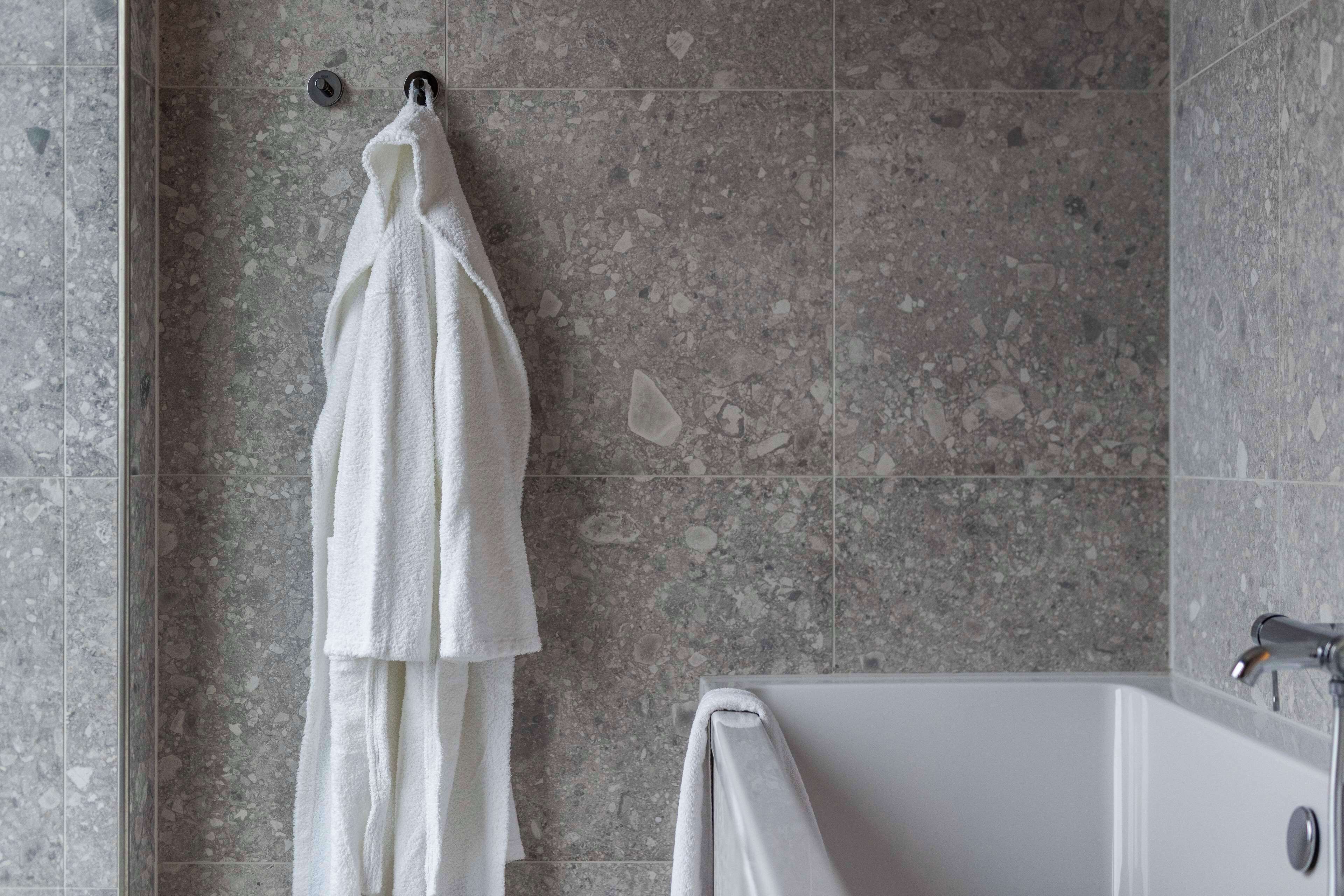 Un baño con una bañera blanca, una toalla colgada de un perchero y paredes de azulejos con vetas.