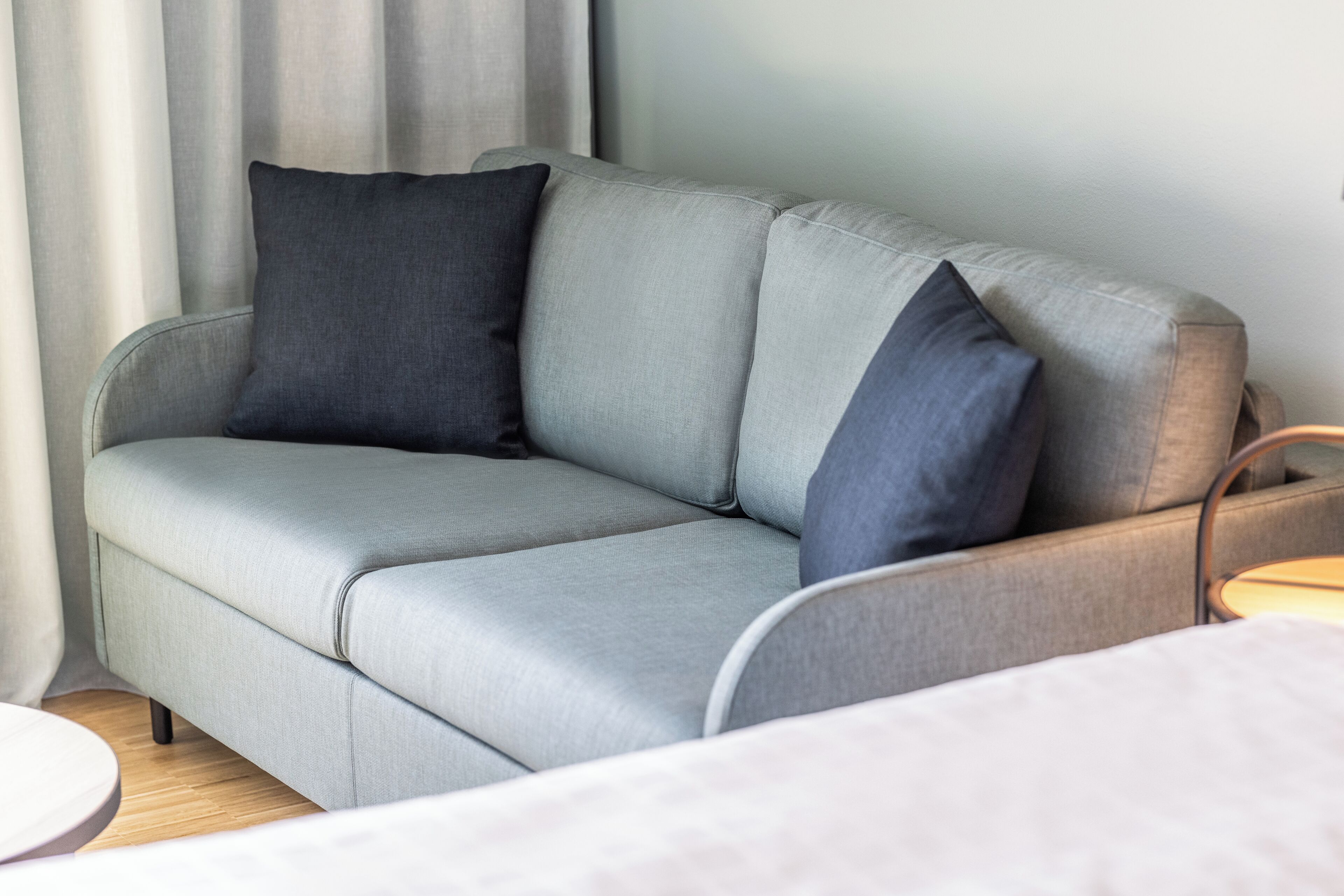 A grey sofa with dark cushions in a room with a wooden floor and a round table.