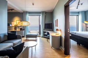 Et moderne hotelværelse med en sofa, et lille bord, et skrivebord, et fjernsyn og en seng.