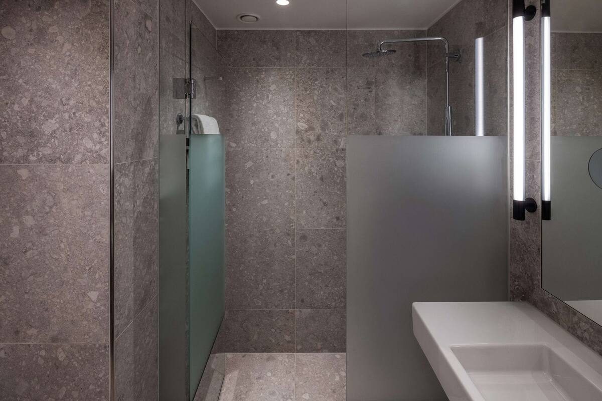 A modern bathroom with a glass shower enclosure, a white sink, and a marble-tiled wall.