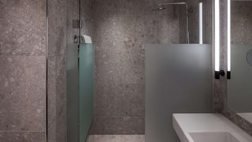 A modern bathroom with a glass shower enclosure, a white sink, and a marble-tiled wall.