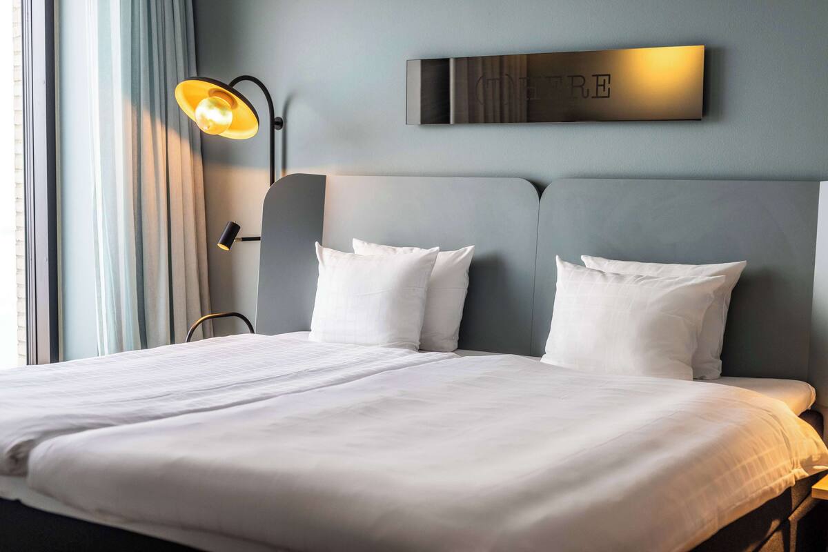 A neatly made bed with white linens in a hotel room.