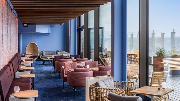 A rooftop bar with seating areas, including sofas and chairs, and large windows offering a view of the sea. - Scandic CPH Strandpark (Kastrup)