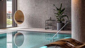 A modern indoor pool with clear water, a hanging wicker chair, a potted plant, and a metal cart with a kettle. - Scandic CPH Strandpark (Kastrup)