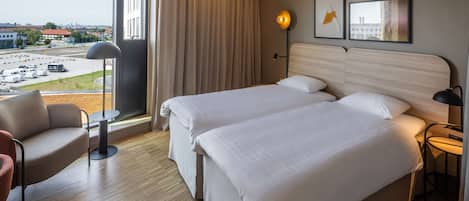 A hotel room with two beds, a view of a parking lot, a chair, and a lamp.