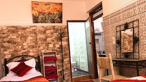 Una camera da letto con parete in pietra, un letto con biancheria rossa e bianca, uno scaffale con asciugamani piegati, una sedia e un grande specchio.