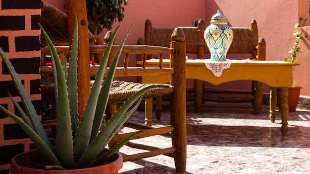 Un patio con un tavolo e sedie di legno, una pianta di aloe in vaso e un vaso decorativo.