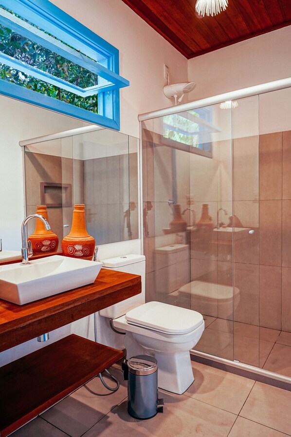 A modern bathroom with a glass shower enclosure, a white sink, and two decorative orange vases on a wooden countertop. - Pousada Aqualtune (Maraú)
