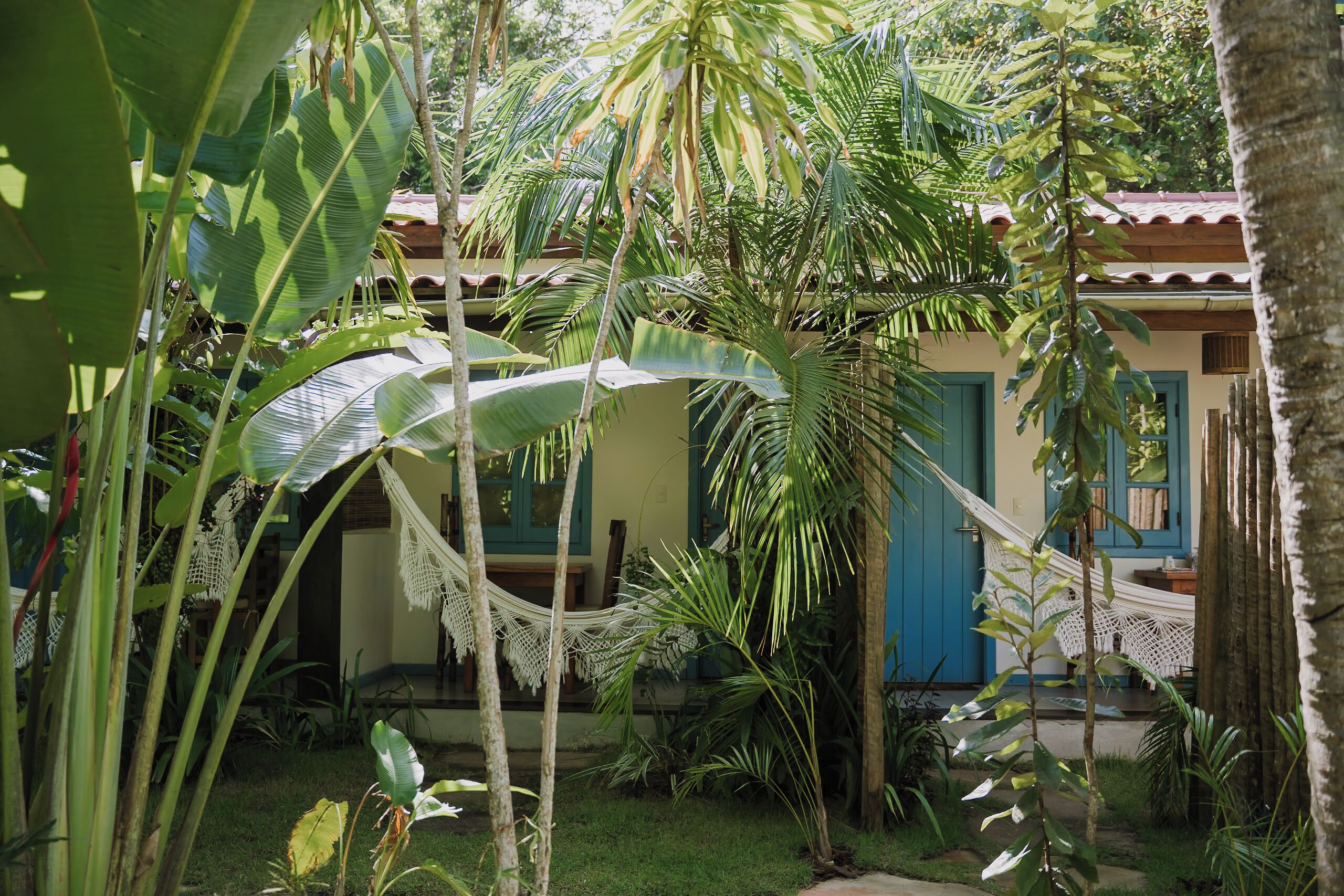 Un jardín tropical con hamacas, un edificio con puertas azules y abundante vegetación.