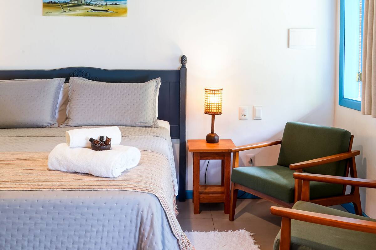 A bedroom with a bed, a nightstand, a lamp, a chair, and a painting on the wall.
