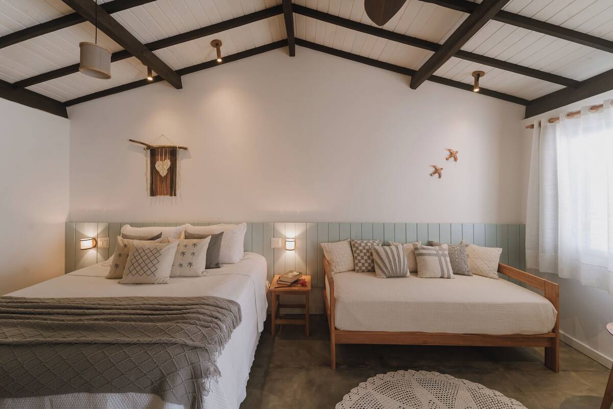 A bedroom with two beds, wooden beams, a hanging light fixture, wall-mounted lights, and a small table with books.